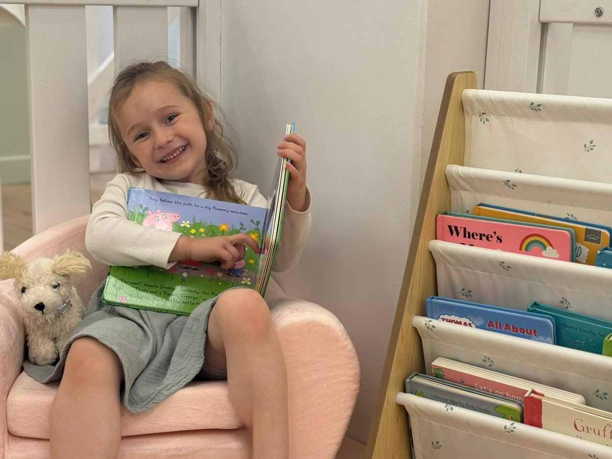 A child reading a picture book beside the face-out book shelves at Butterfly & Bee Books